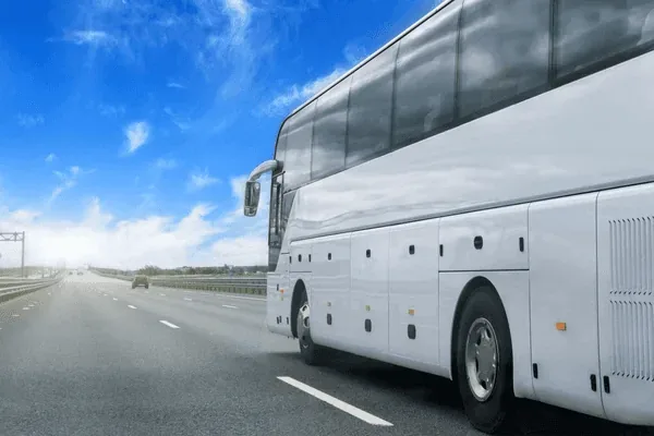 A sleek, white tour bus traveling on a wide, open highway under a bright blue sky with scattered clouds.