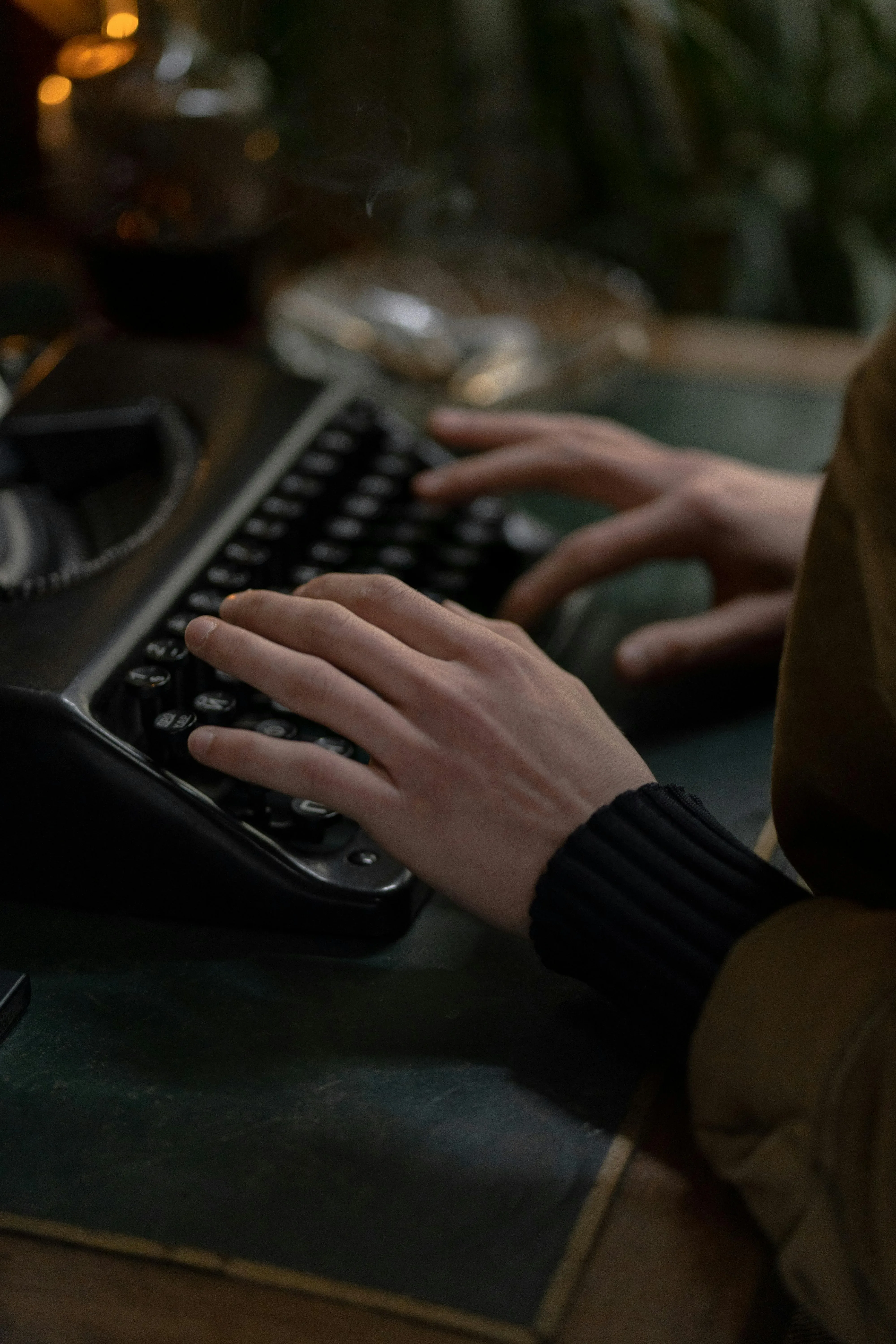 A person types on a vintage typewriter, their fingers poised over the keys, with dimly lit surroundings and a warm, cozy atmosphere.